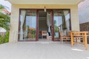Entrada de hotel con el número '5' sobre la puerta, un patio cubierto con sillas de madera y una pequeña mesa.
