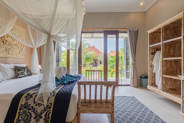 A bedroom with a bed, a wooden chair, a wardrobe, and a view of the outside garden. - Favorit Bungalows (Penida Island)