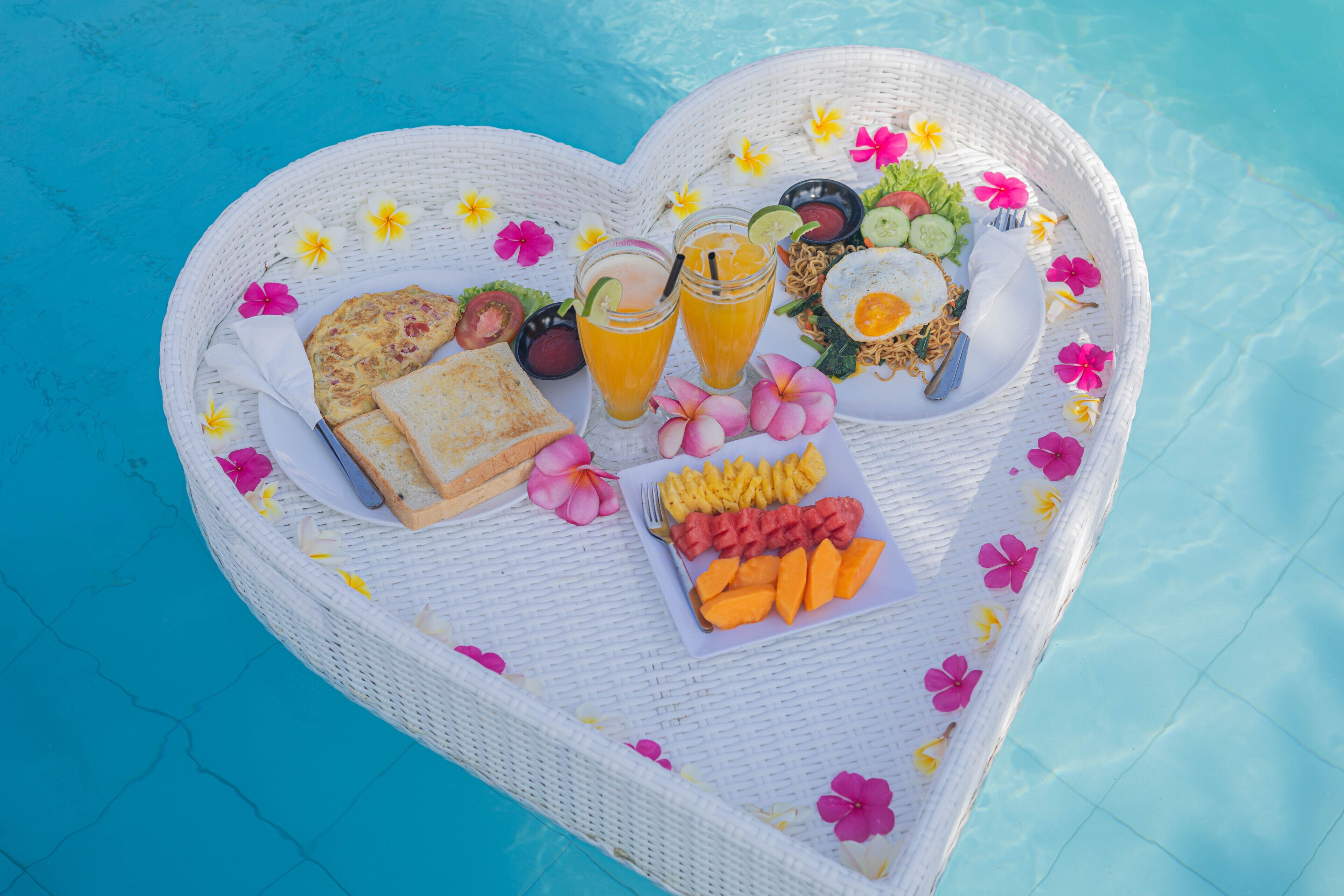 A heart-shaped tray with food and drinks by a pool.