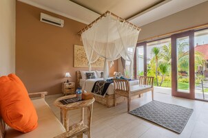 Un dormitorio con cama a dosel, una silla de madera, una mesita y vistas a un jardín tropical.