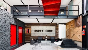 Een moderne lobby met een 'SWEET-HOME' bord, zwarte en rode deuren, een houten wand en een trap naar een hoger niveau.