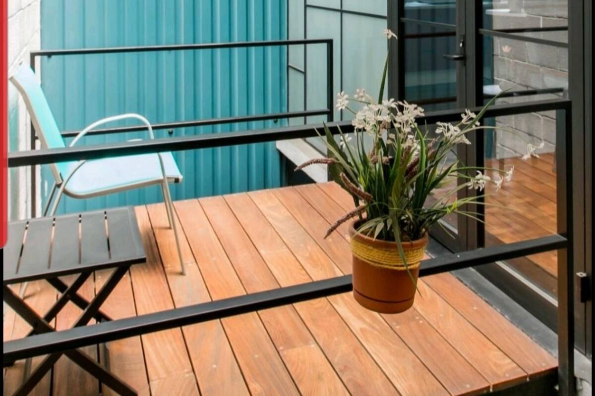 A wooden deck with a table and chairs, two hanging planters with plants, and a blue corrugated wall.
