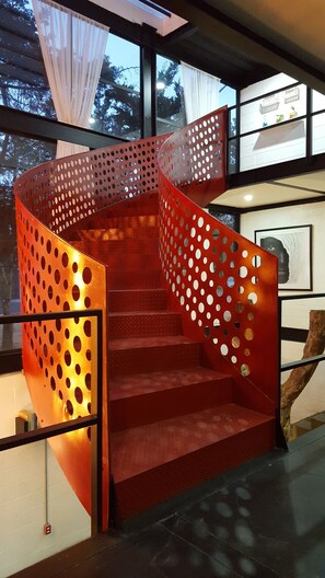 Una escalera de caracol con barandillas de metal rojo y paneles perforados, que conduce a un piso superior.