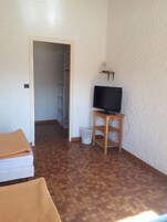 A small room with a tiled floor, a television on a wooden stand, a white door, and a small white trash bin.