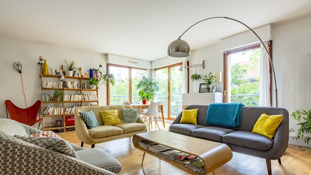 En moderne stue med en sofa, lænestol og sofabord. Der er et bogreol fyldt med bøger og pynteting.