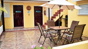 Een terras buiten met een tafel, stoelen, een welkomstbord en een brandblusser.