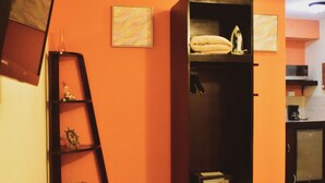 Een kamer met een houten stoel, een zwarte plankenwand met een klein tafeltje, en een keuken op de achtergrond.
