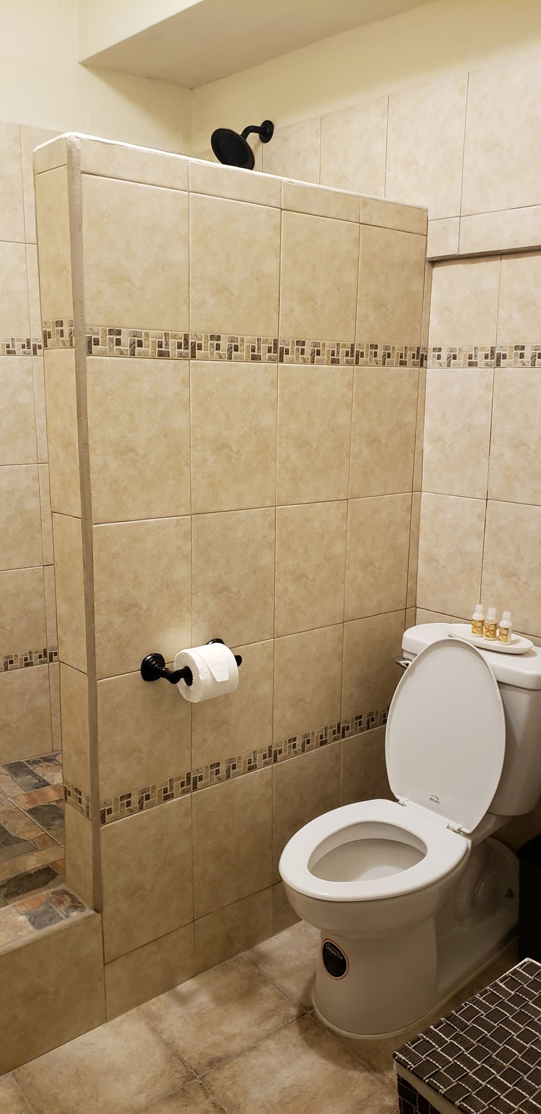 A bathroom with beige tiles, a toilet, a shower area, and a toilet paper holder.