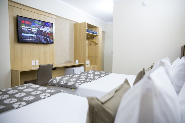 A hotel room with two beds, a desk, a chair, a TV mounted on the wall, and a wardrobe. - Allcon House Inn Hotel AnaShopping By Perfecta Hotels (Anapolis)