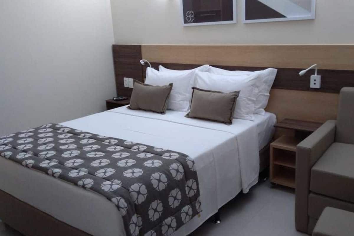 Ein Hotelzimmer mit einem Bett, einem Nachttisch, einem Stuhl und einer Wandleuchte.