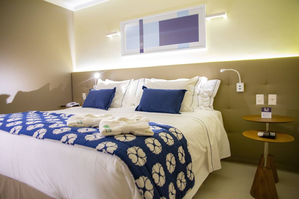 Ein Hotelzimmer mit Bett, Nachttisch und an der Wand montiertem Fernseher.