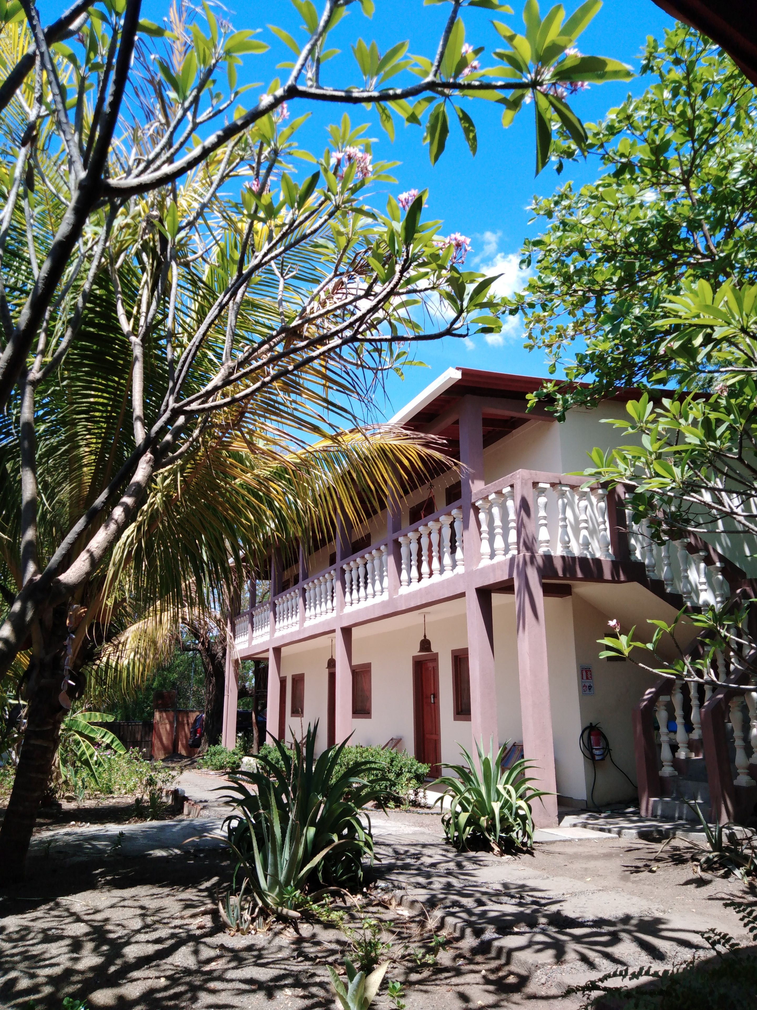 Un edificio tradicional con balcón, rodeado de exuberante follaje y palmeras.