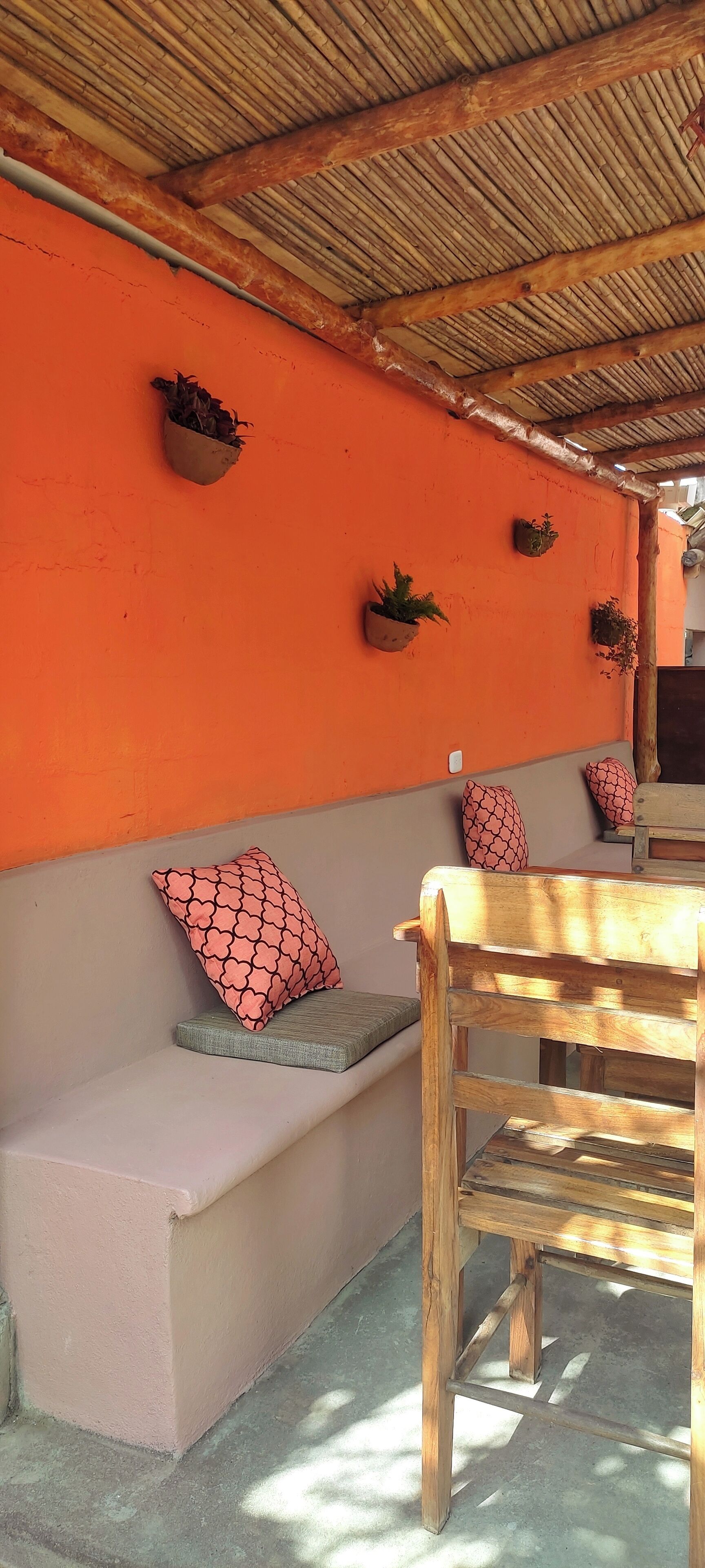 Un banco de madera y un banco con cojín rojo estampado frente a una pared naranja.