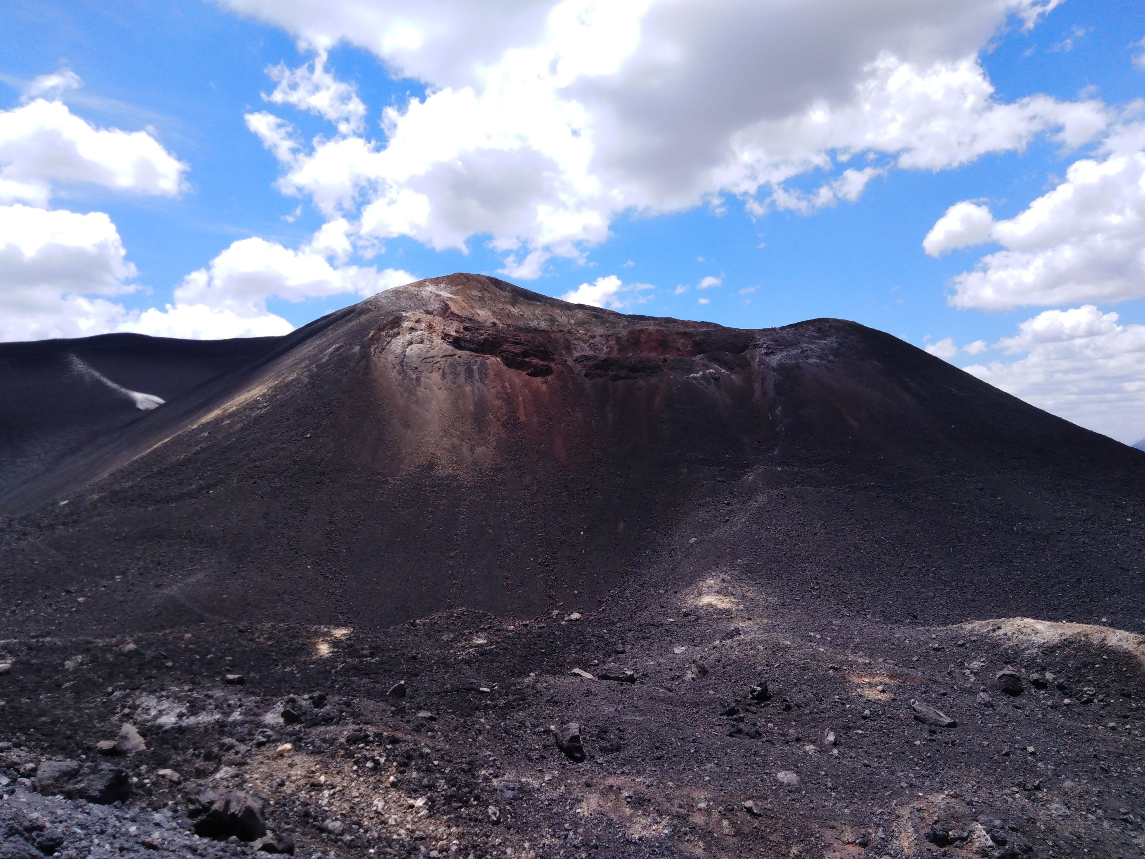 Ett vulkaniskt landskap med en krater, stenigt område och en klar himmel.
