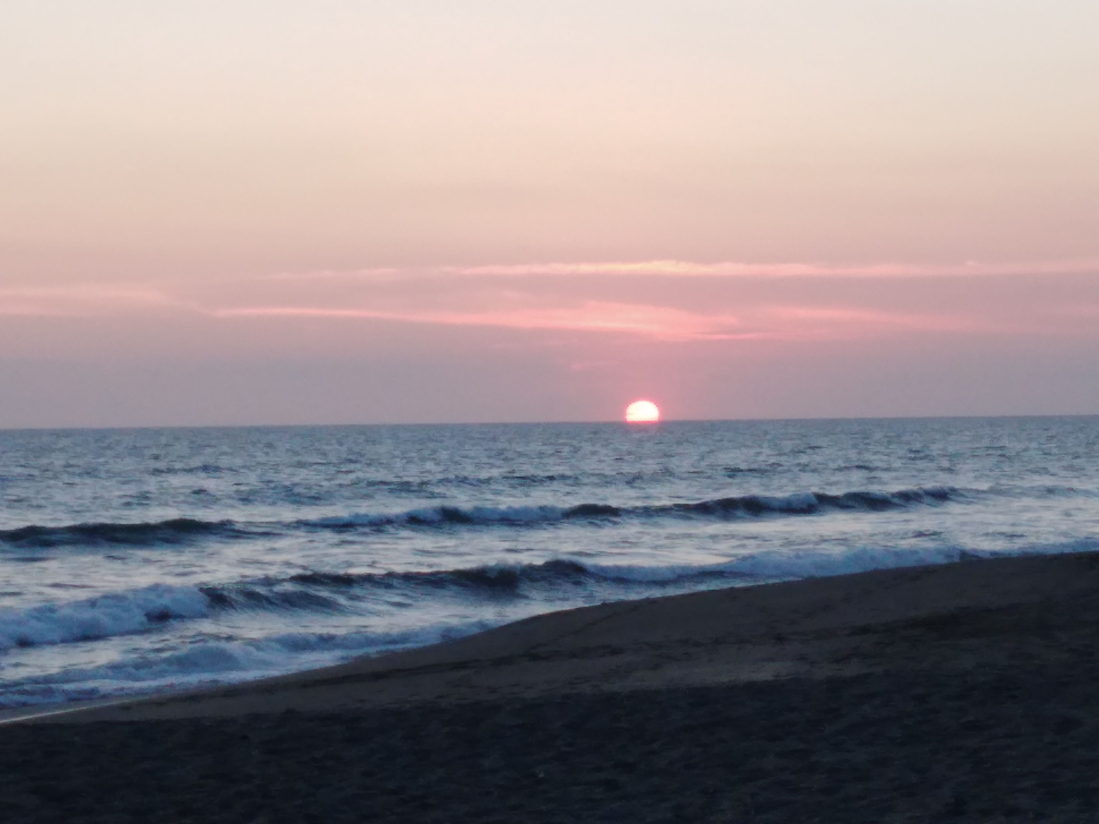 Una playa con olas y un atardecer a lo lejos.