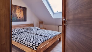 Ein Schlafzimmer mit geneigter Decke, einem Oberlicht, einem Bett mit geometrischem Muster, einem hölzernen Kopfteil, einem Bild an der Wand und einem Sessel.