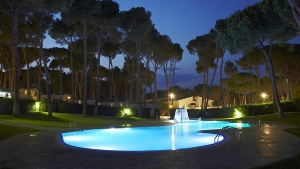 A swimming pool at dusk with surrounding trees and a building in the background. - Camping Interpals (Pals)