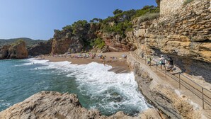 A coastal beach with rocky cliffs, a stone pathway, and beachgoers. - Camping Interpals (Pals)