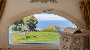 A room with a large arched window offering a view of a grassy area and the sea.