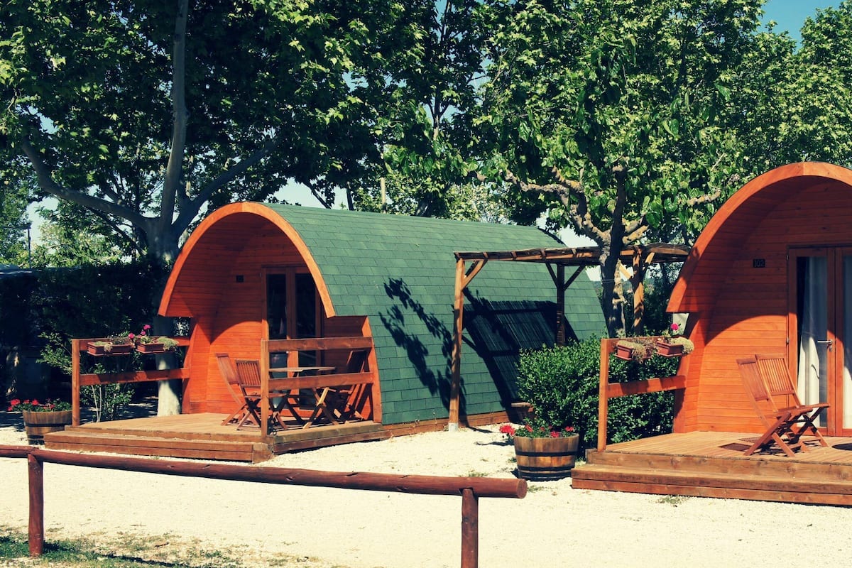 Two wooden cabins with green roofs, each featuring a wooden deck and seating area.