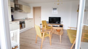 Een moderne keuken met houten kastjes, een inbouwoven en een eethoek met gele stoelen en een ronde tafel.
