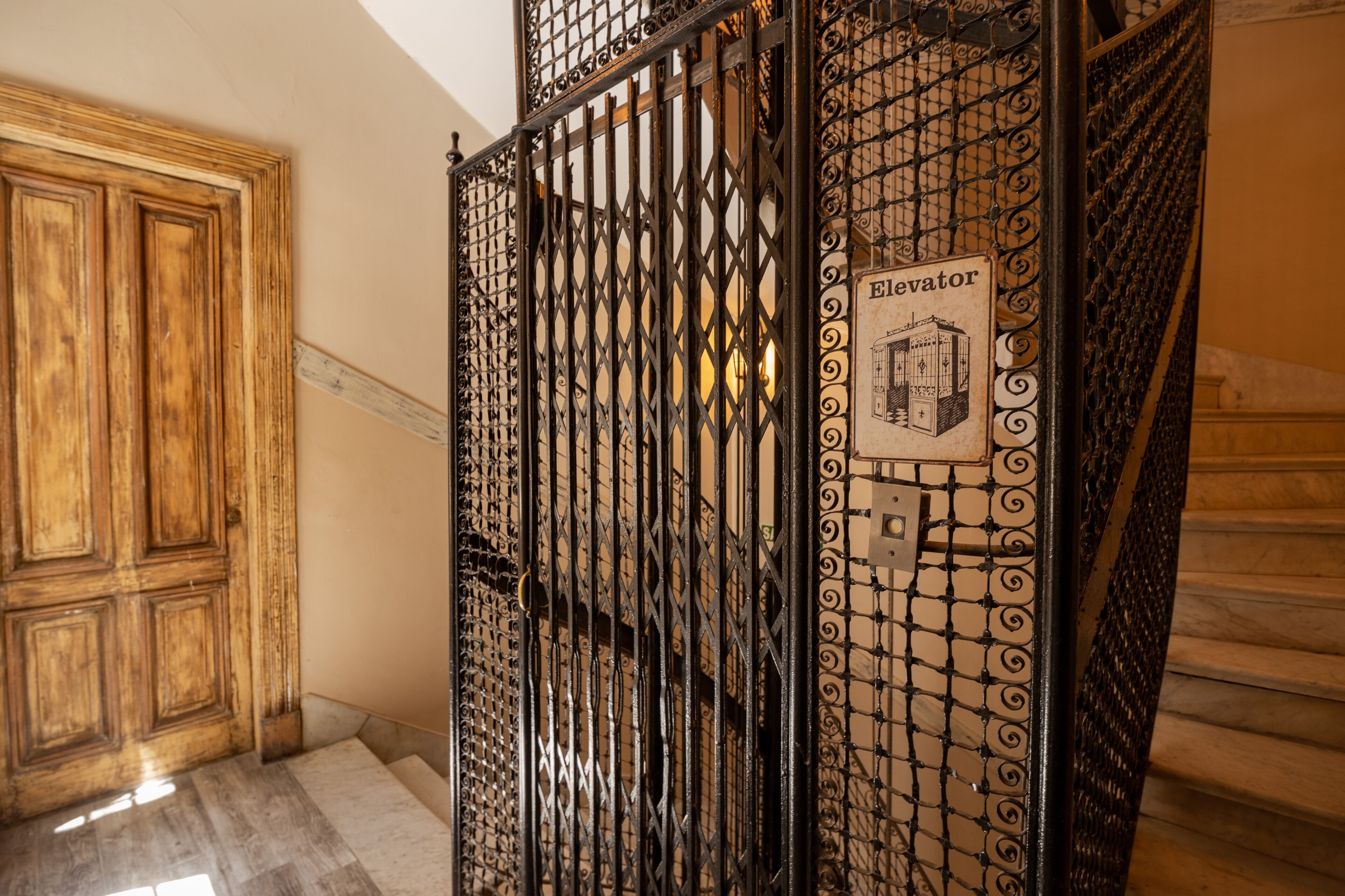 Un escalier orné d’une grille en fer forgé et d’une indication signalant la présence d’un ascenseur.