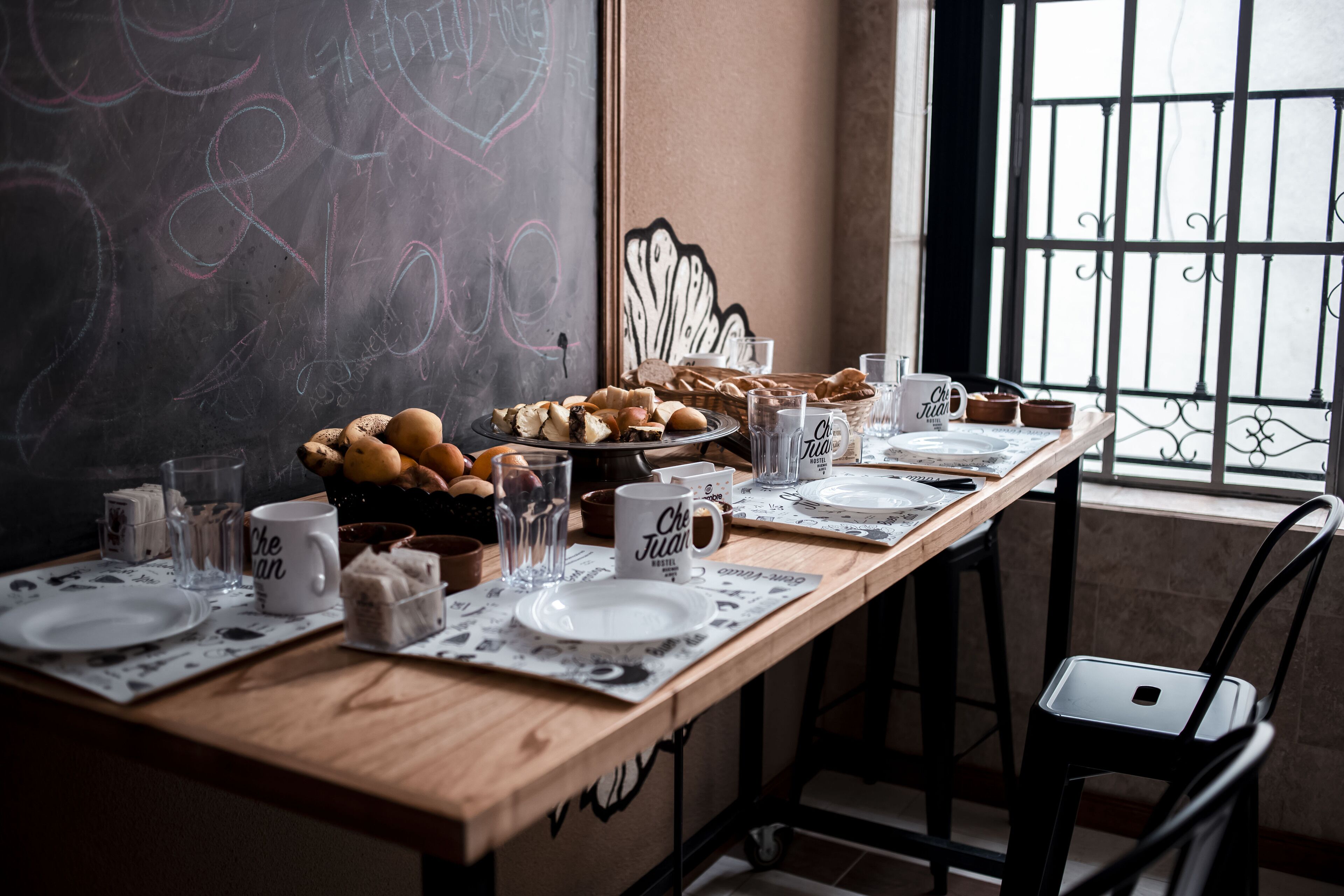 A breakfast setting with a wooden table, plates, cups, and a chalkboard with writing.