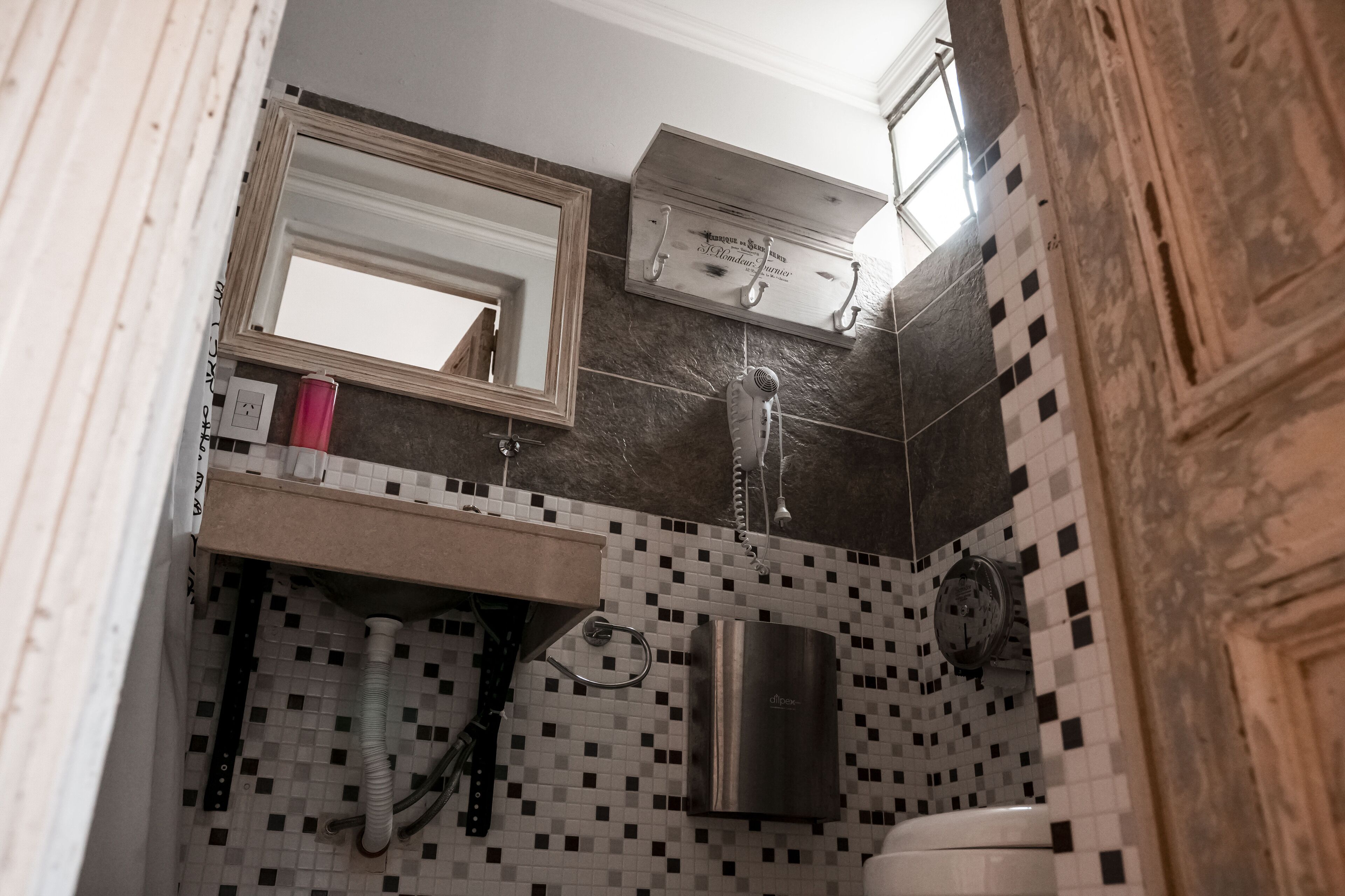 Un baño con salpicadero de azulejos, un espejo, un perchero para toallas, un secador de pelo y un lavabo.
