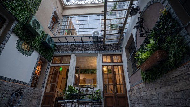 A courtyard with a wooden table and chairs, surrounded by stone walls and potted plants. - Che Juan Hostel BA (Buenos Aires)