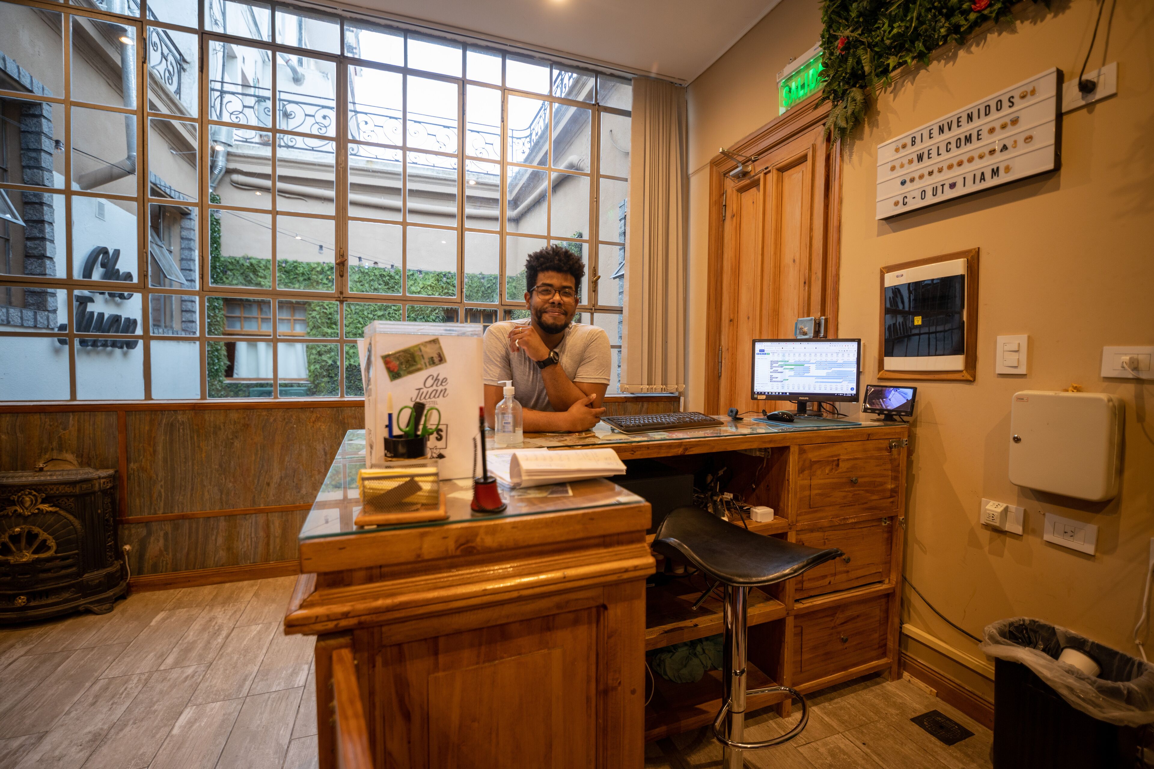 Un mostrador de recepción con una computadora, un letrero que dice 'Bienvenidos Welcome' y vistas al exterior a través de amplias ventanas.