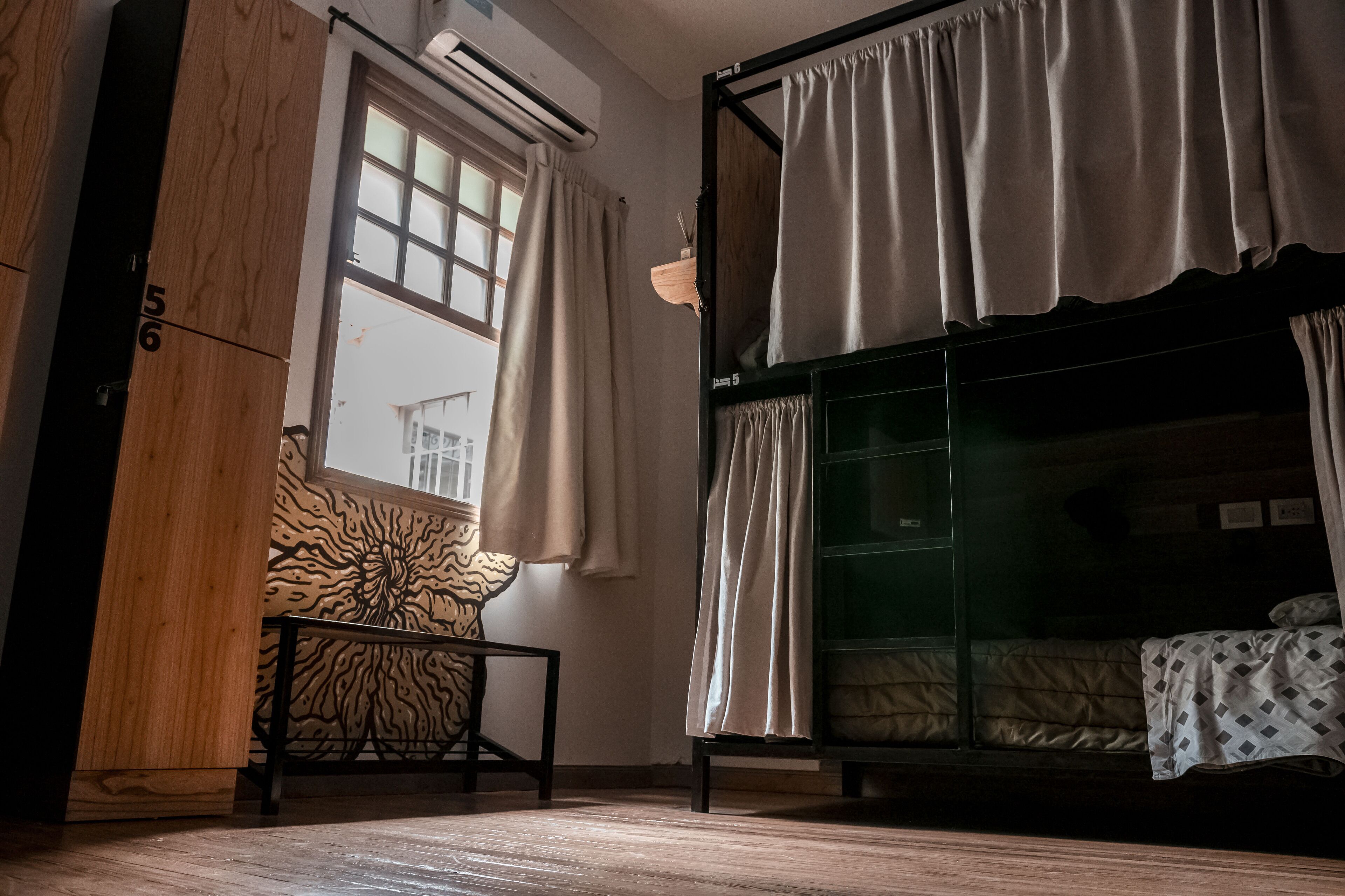 Une chambre avec un lit superposé, une fenêtre avec des rideaux, un climatiseur fixé au mur et un mur décoré d’un motif.