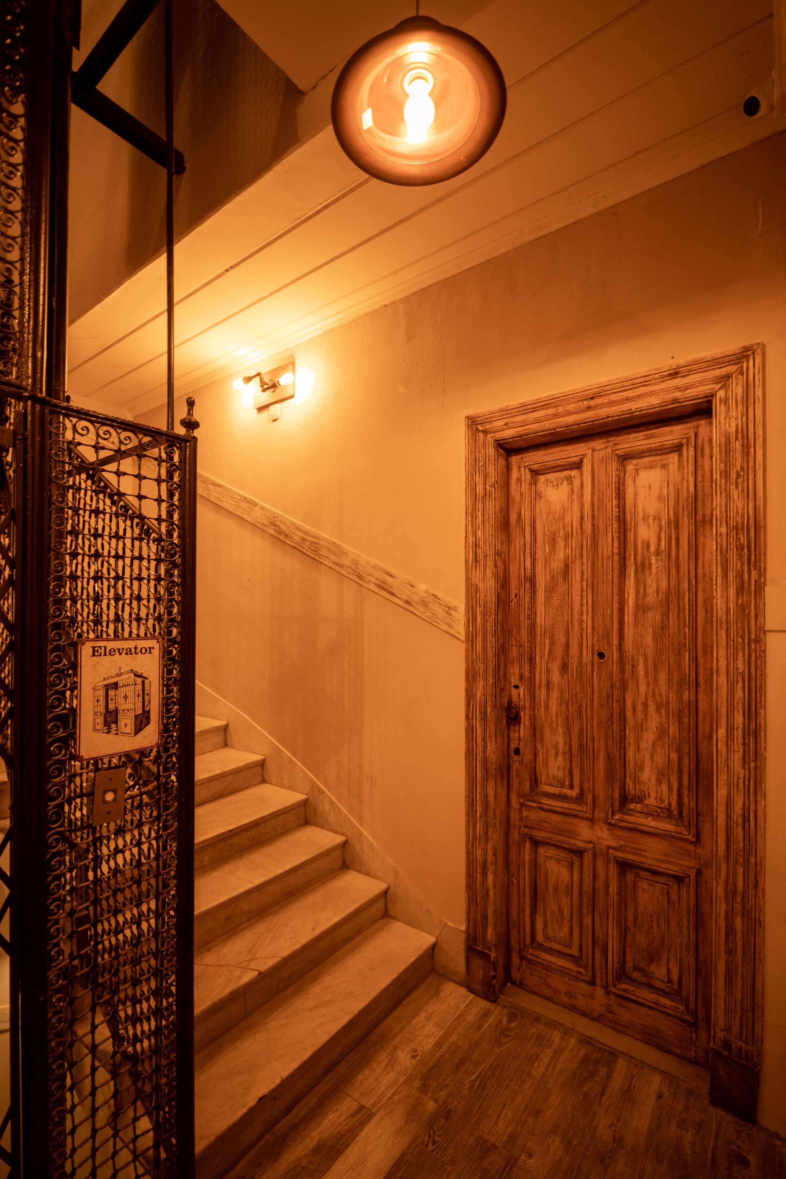 A staircase with a wooden door at the end, a metal gate with an 'Elevator' sign, and a wall-mounted light fixture.