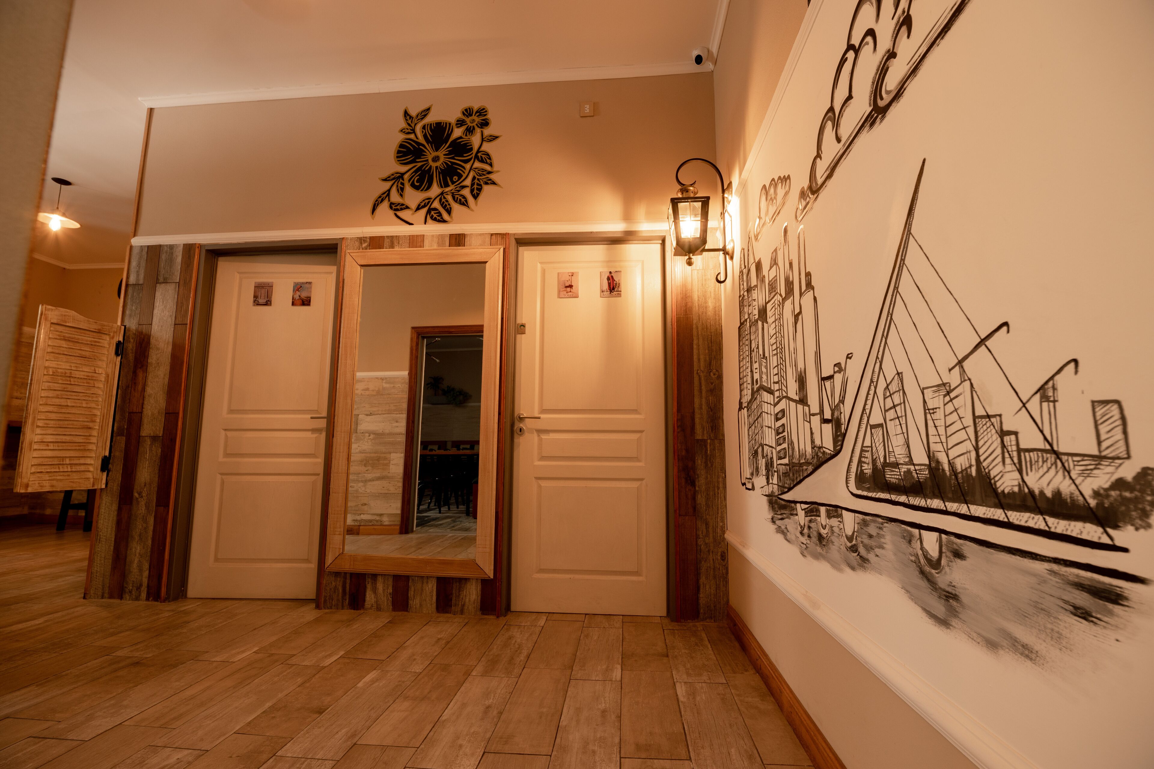 Een gang met houten vloer, een wandlamp en een groot muurdecoratie van een brug.