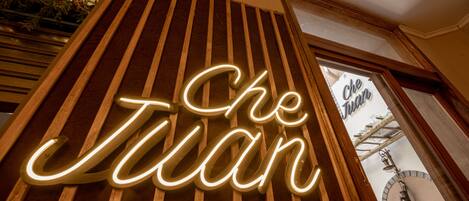 A neon sign spelling "Che Juan" on a wooden slat wall.