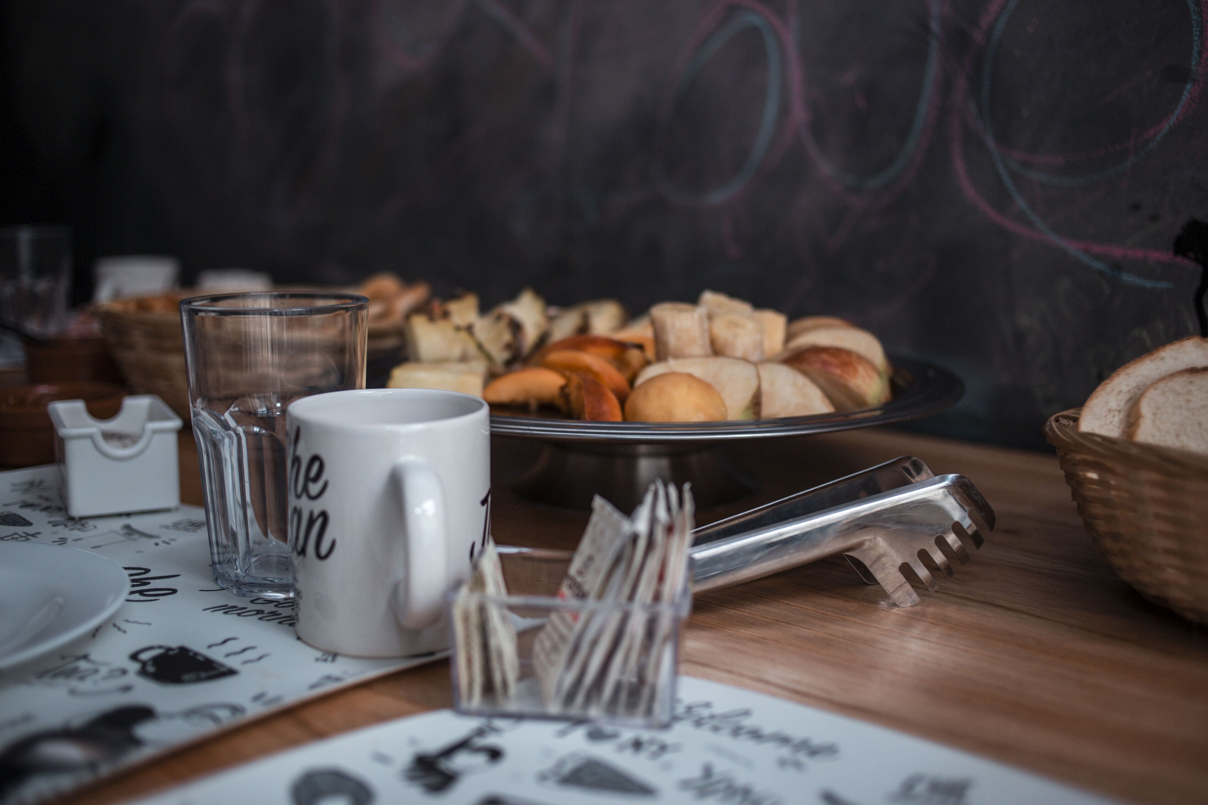 Una mesa con una fuente de pan, un vaso, una taza y un periódico.