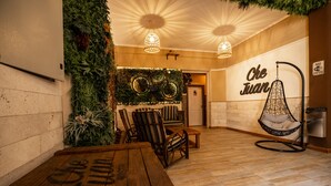 A cozy indoor space with a wooden table, chairs, a hanging chair, and a wall with greenery and a sign that reads "Che Juan". - Che Juan Hostel BA (Buenos Aires)