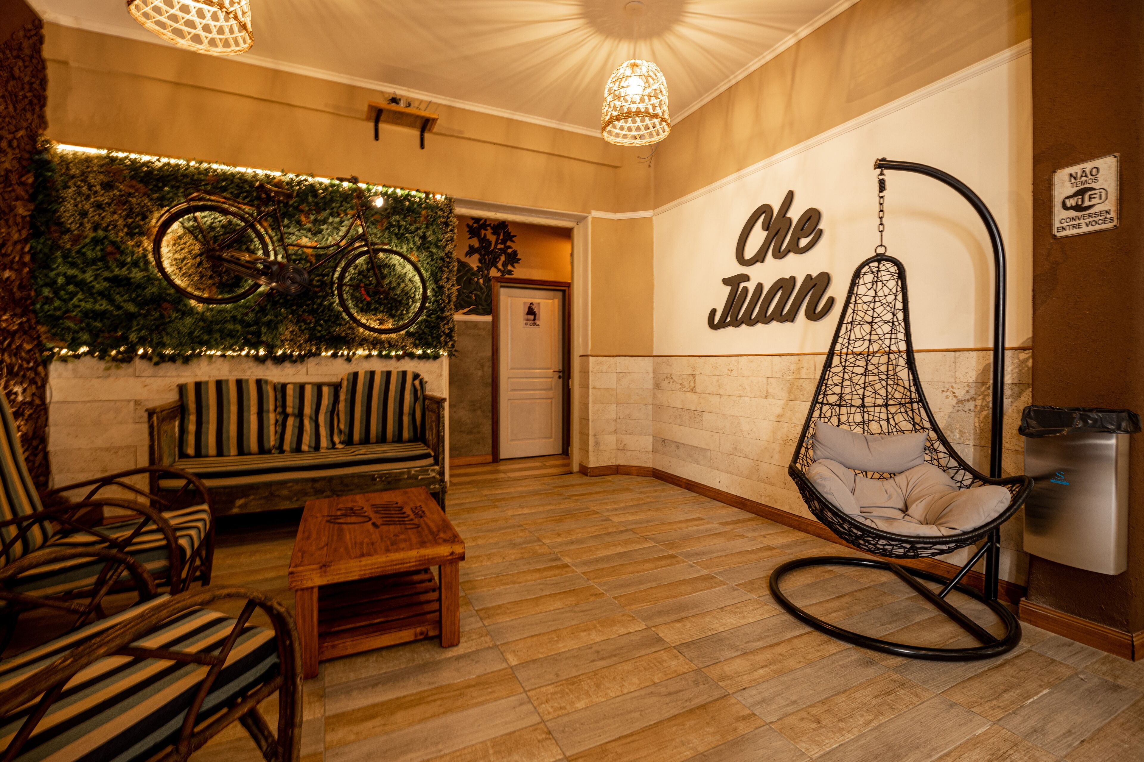 A lobby with a wooden floor, a hanging chair, a sofa, and a wall-mounted sign reading "Che Juan".