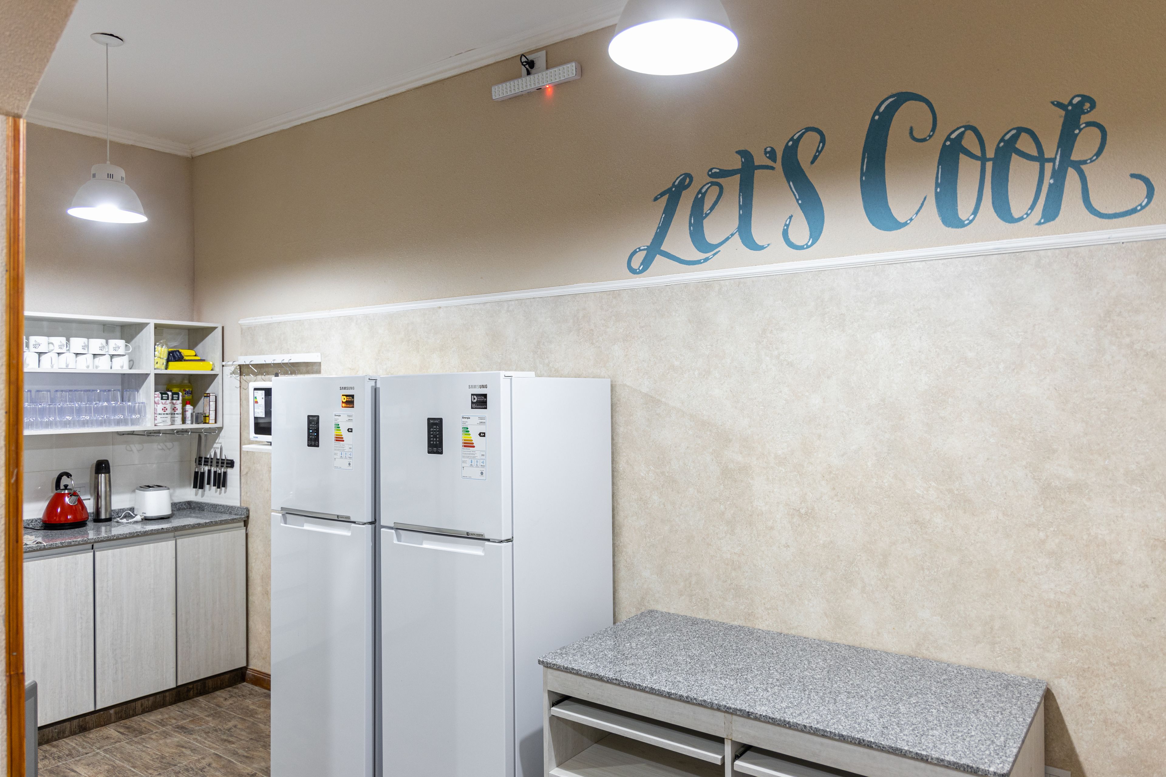 A modern kitchen with two white refrigerators, a granite countertop, and a 'Let's Cook' sign on the wall.