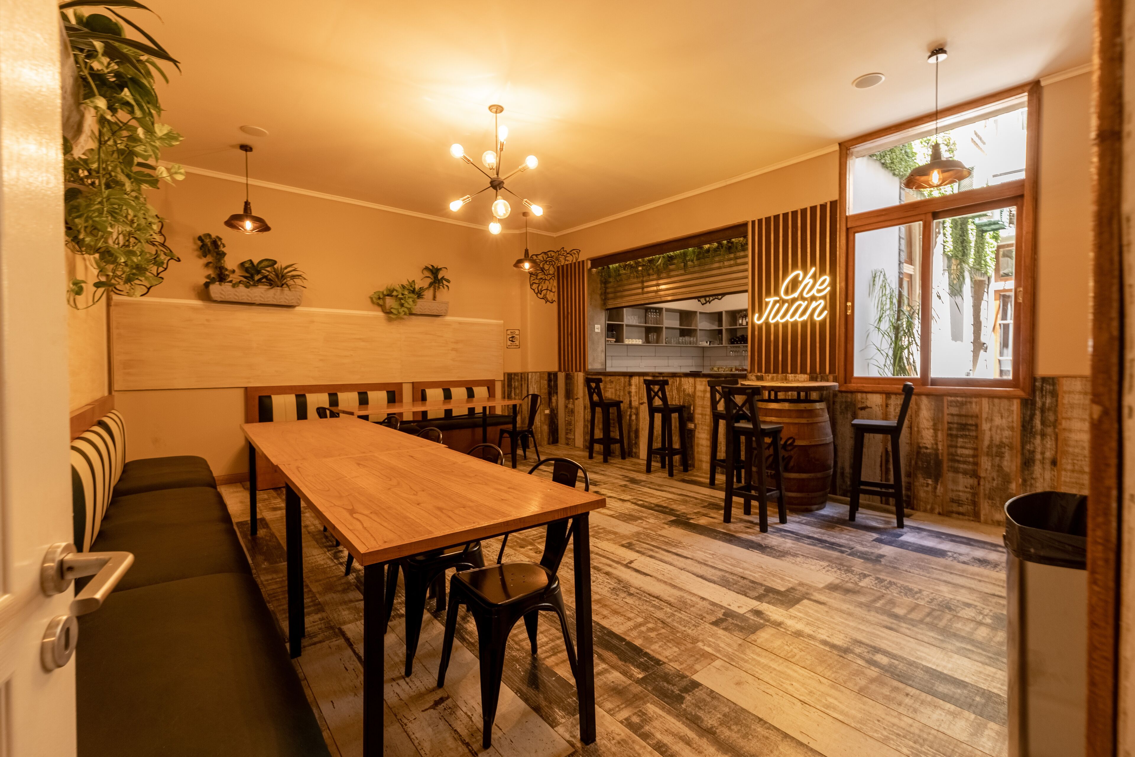 A cozy restaurant with a wooden table and benches, a bar area, and large windows with a view of the street.