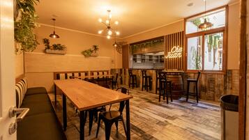 A cozy restaurant with a wooden table and benches, a bar area, and large windows with a view of the street.