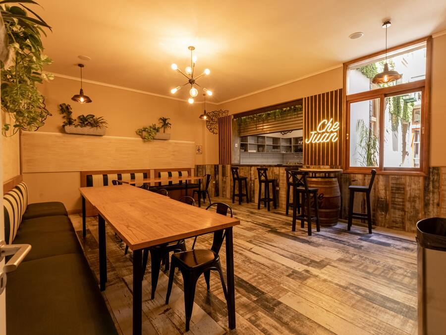 A cozy restaurant with a wooden table and benches, a bar area, and large windows with a view of the street.