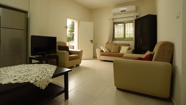 A living room with a television, sofa, and a table with a lace tablecloth. - The Garden Apartment (Nazareth)