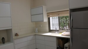 A kitchen with white cabinets, a window with a view, and a refrigerator. - The Garden Apartment (Nazareth)