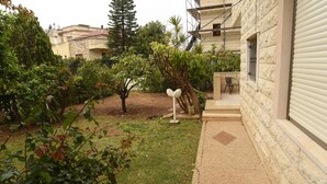 A courtyard with a small garden, a white mailbox, and a building with a stone facade and a window with a metal grille. - The Garden Apartment (Nazareth)