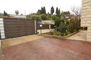 A paved driveway leading to a gated entrance, surrounded by a garden with various plants and a street lamp.