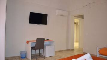 Habitación de hotel con cama, escritorio, silla, televisor y aire acondicionado.