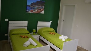 A room with two beds, green walls, and a painting of a coastal scene. - B&B Stella Maris Trapani Centro (Trapani)
