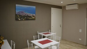 A dining area with two white tables and chairs, a painting of a coastal landscape, and an air conditioning unit on the wall. - B&B Stella Maris Trapani Centro (Trapani)