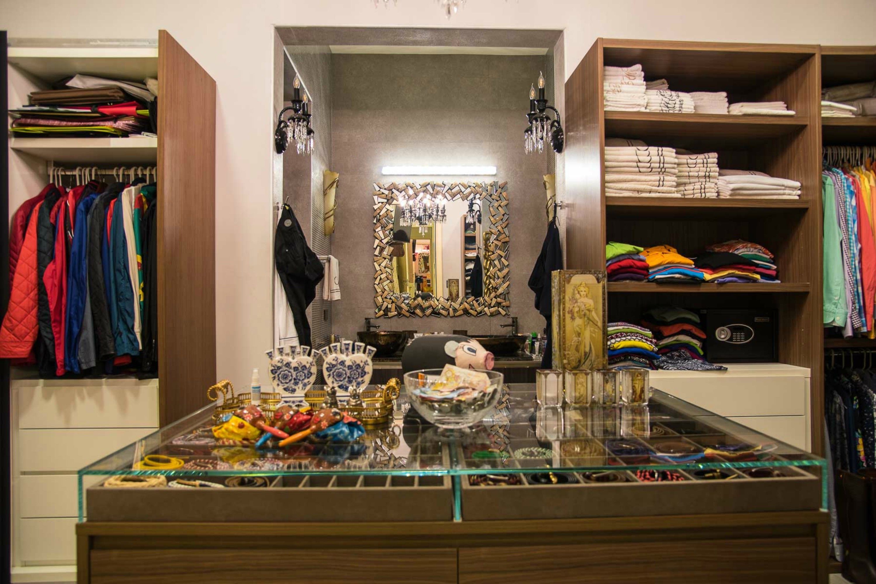 Una habitación con una vitrina de vidrio llena de varios objetos, un espejo con marco decorativo y estantes con ropa doblada.
