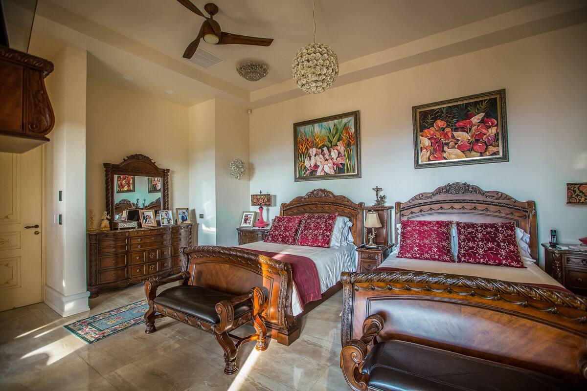 A spacious bedroom with two ornate wooden beds, a large mirror, and a ceiling fan.